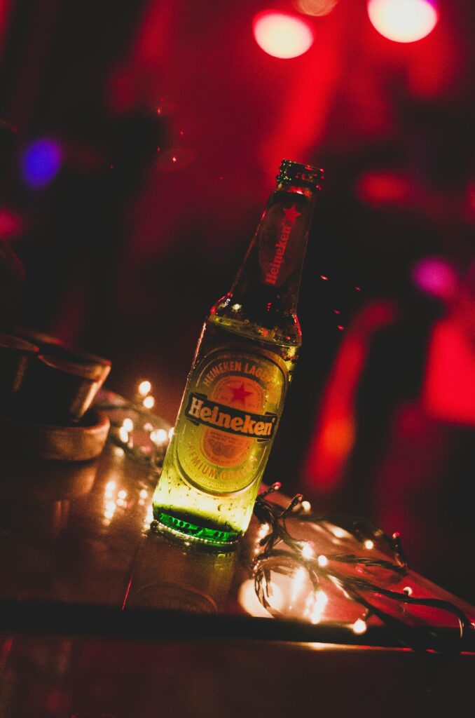 Close-up of a Heineken beer bottle illuminated by string lights in a vibrant party setting.